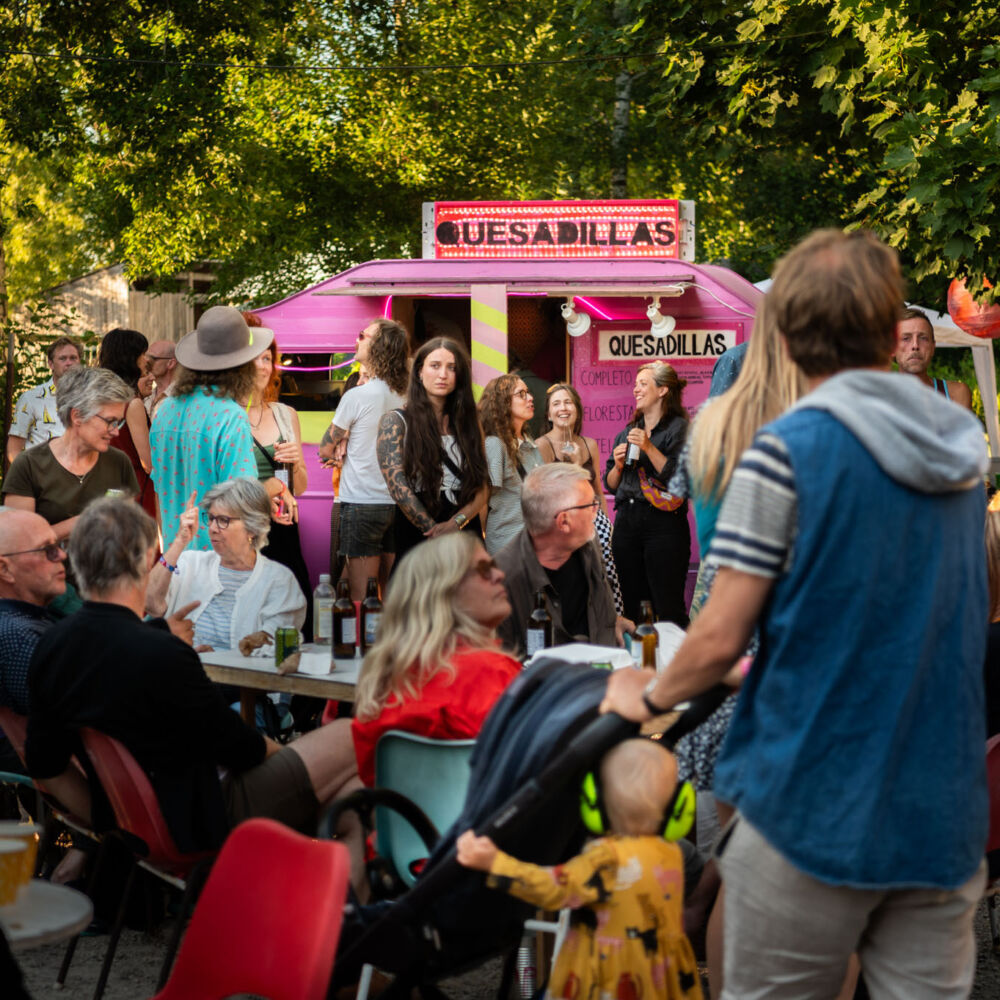 People gathered by a pink food truck outdoors.